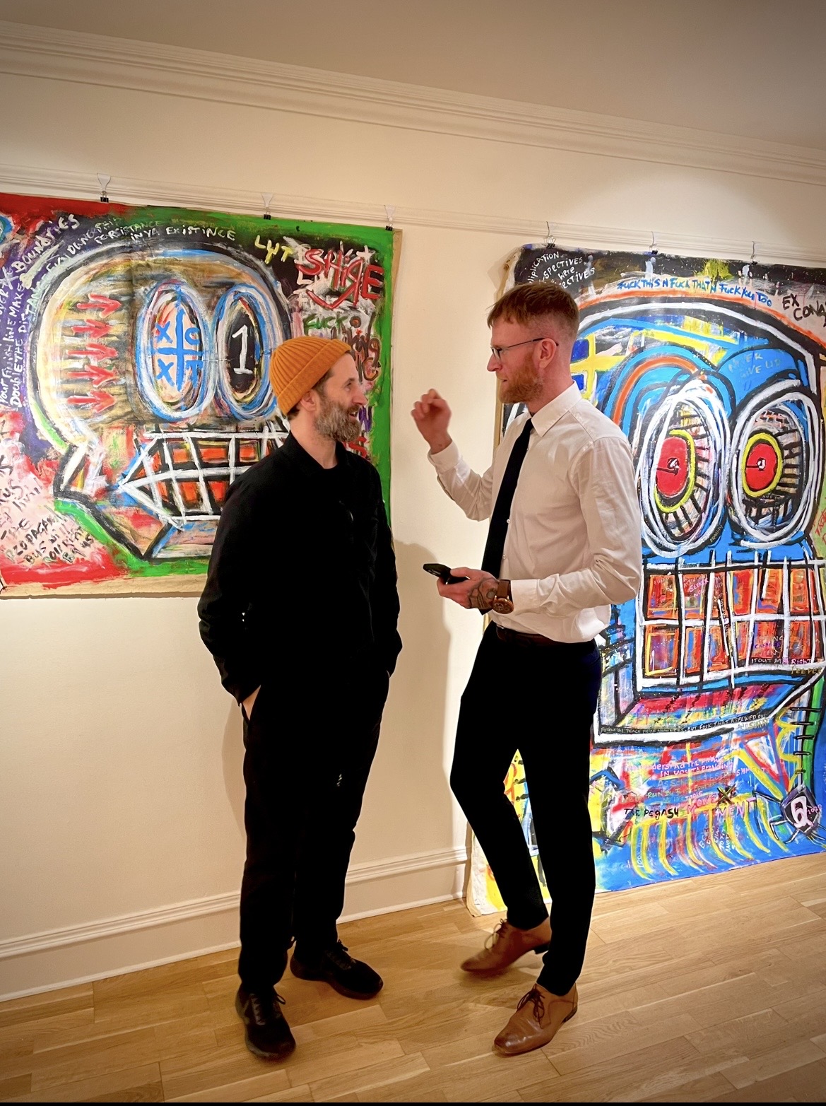 R.P. Gribben in conversation with a visitor beside two large exhibited paintings