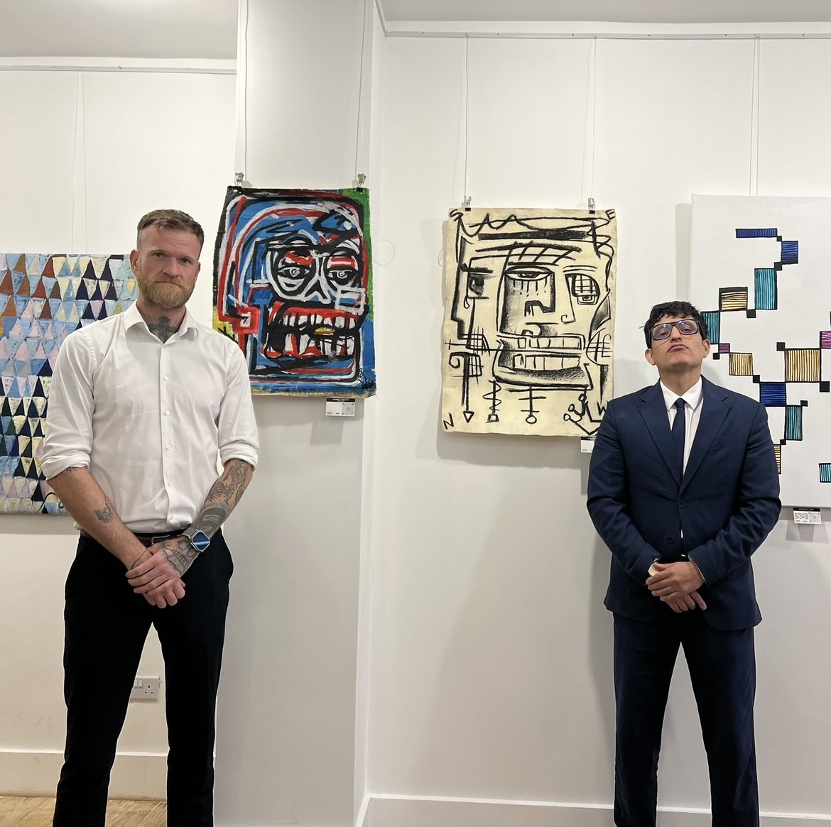 R.P. Gribben standing in a group exhibition with paintings installed behind him